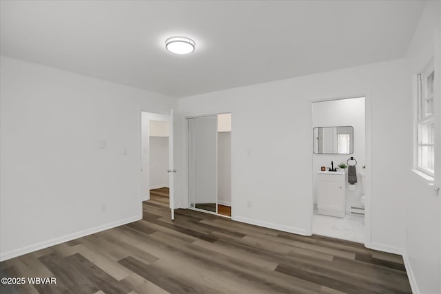 unfurnished room featuring sink, a baseboard heating unit, and dark hardwood / wood-style flooring