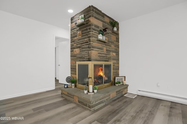 interior details featuring hardwood / wood-style floors, baseboard heating, and a stone fireplace