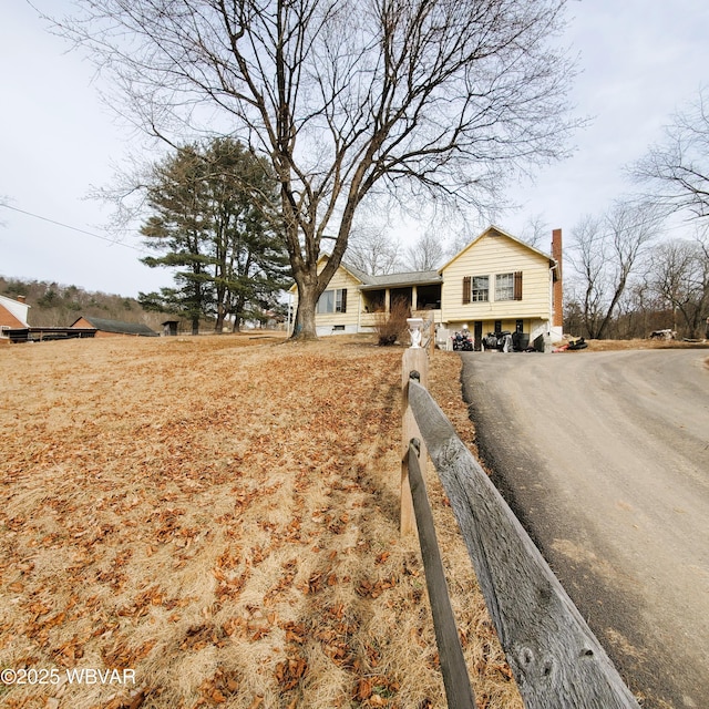 view of front facade featuring driveway, a chimney, and fence