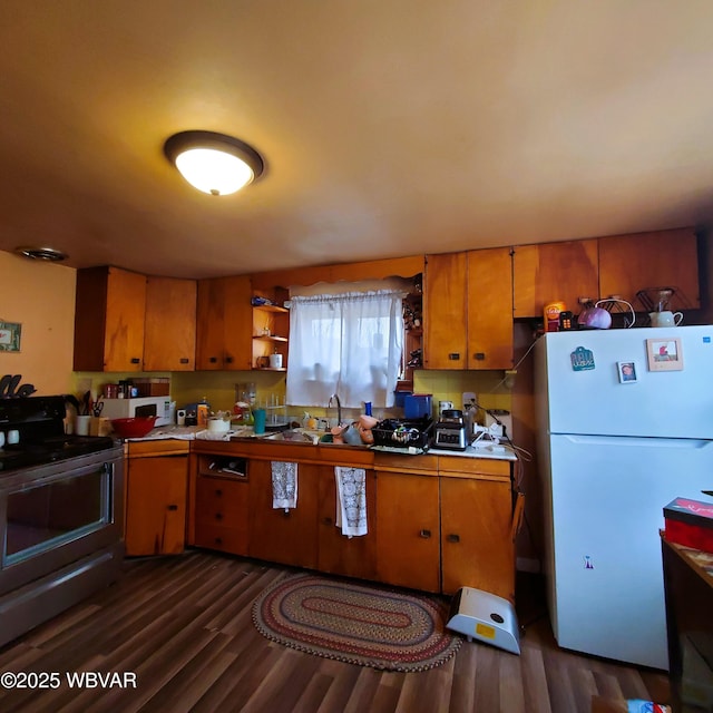 kitchen featuring dark wood-style floors, light countertops, black electric range oven, freestanding refrigerator, and a sink