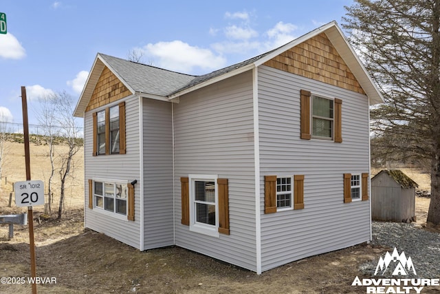 view of side of property with a storage shed, an outdoor structure, and a shingled roof