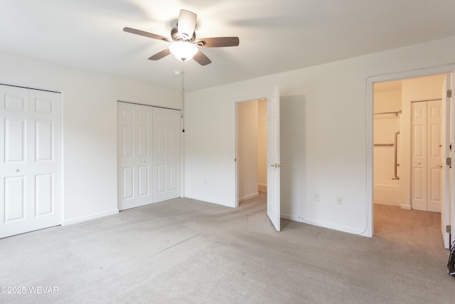 unfurnished bedroom featuring light carpet, ceiling fan, and multiple closets