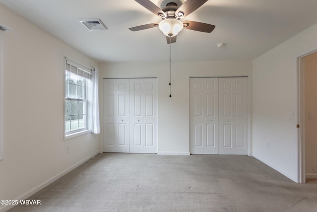 unfurnished bedroom featuring ceiling fan, light colored carpet, and two closets