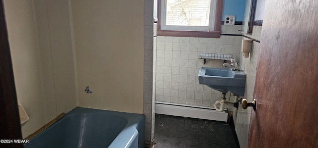 bathroom with tile walls, baseboard heating, a bathing tub, and sink