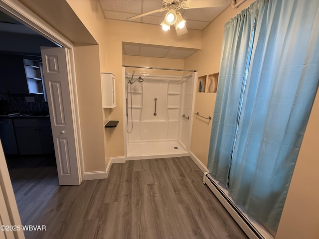 bathroom featuring a shower, a baseboard heating unit, hardwood / wood-style flooring, ceiling fan, and a drop ceiling