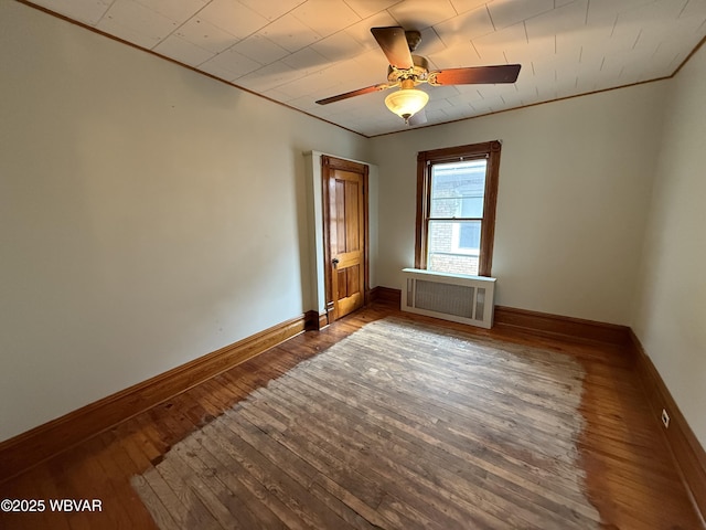 empty room featuring crown molding, ceiling fan, radiator heating unit, and dark hardwood / wood-style floors