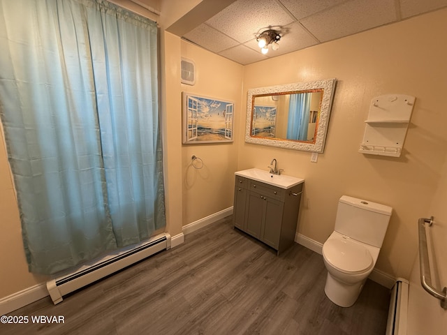 bathroom featuring a baseboard heating unit, hardwood / wood-style flooring, a paneled ceiling, and toilet