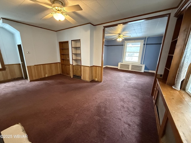 interior space featuring crown molding, radiator, dark carpet, built in features, and ceiling fan