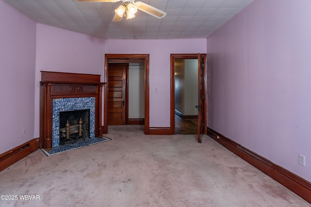 unfurnished living room with a tiled fireplace, light carpet, and ceiling fan