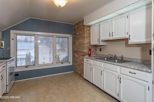 kitchen with vaulted ceiling, brick wall, white electric stove, white cabinetry, and sink