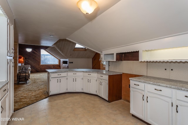 kitchen with white cabinetry, wooden walls, vaulted ceiling, light colored carpet, and kitchen peninsula