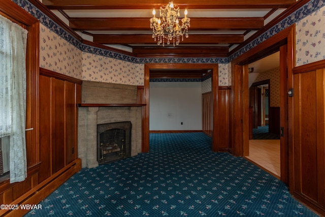 unfurnished living room featuring a chandelier, a baseboard heating unit, dark carpet, a brick fireplace, and beam ceiling