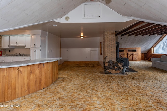 kitchen with sink, lofted ceiling with beams, white cabinets, light colored carpet, and a wood stove