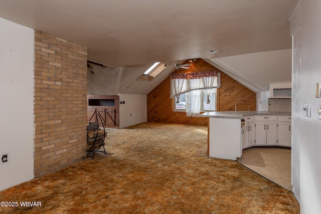 additional living space with lofted ceiling with skylight, light colored carpet, ceiling fan, and wood walls