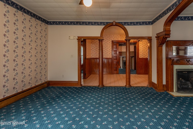 spare room with ornate columns, carpet floors, and wooden walls