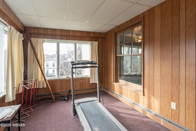 exercise room featuring dark carpet, a drop ceiling, wooden walls, and baseboard heating