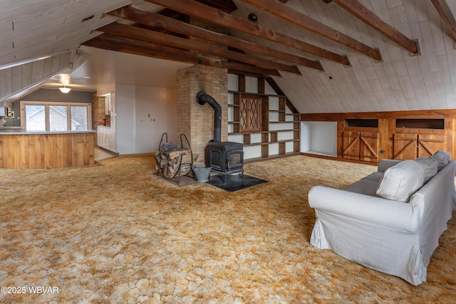 living room featuring wooden walls, lofted ceiling with beams, light carpet, and a wood stove