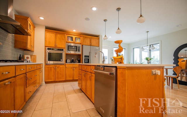 335 Chirlton Pt, Montoursville, PA 17754 - kitchen with stainless steel appliances, wall chimney exhaust hood, brown cabinetry, an island with sink, and tasteful backsplash