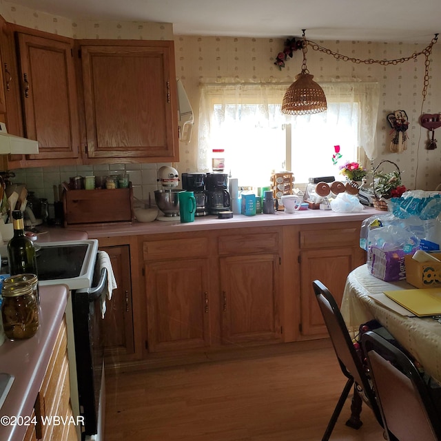 kitchen with hanging light fixtures, black electric range oven, light hardwood / wood-style floors, and decorative backsplash