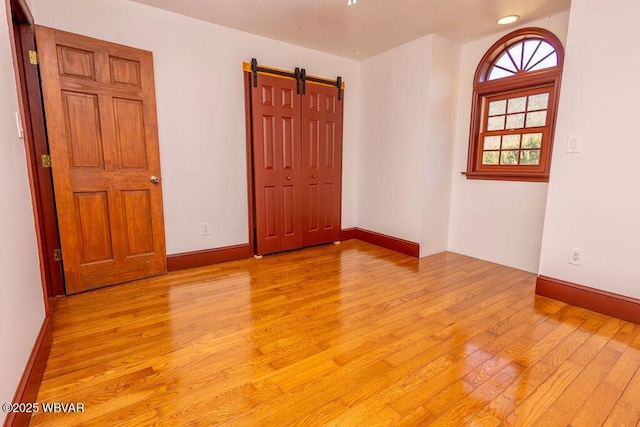 empty room featuring light wood-style flooring, baseboards, and a barn door