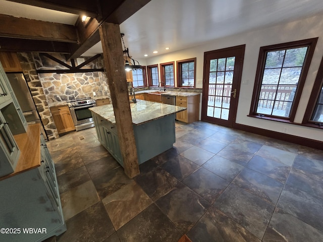 kitchen featuring light stone countertops, baseboards, a kitchen island, a sink, and appliances with stainless steel finishes