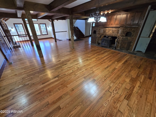 unfurnished living room featuring beam ceiling, an inviting chandelier, wood finished floors, and stairs