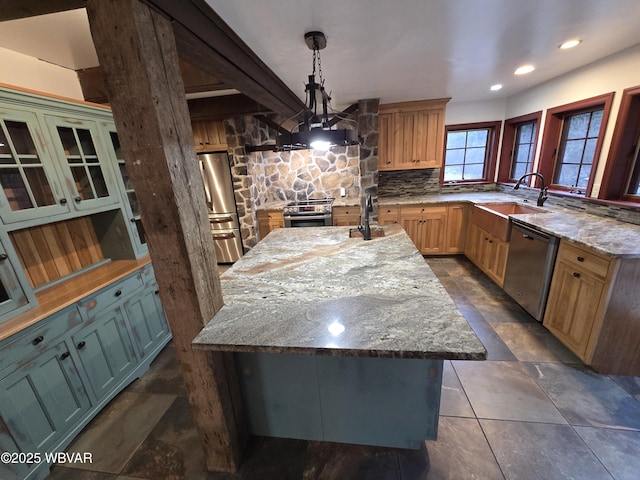 kitchen with light stone countertops, an island with sink, a sink, hanging light fixtures, and stainless steel appliances