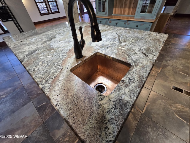 details featuring light stone counters, glass insert cabinets, baseboards, and a sink