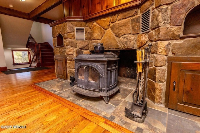 room details featuring visible vents, beamed ceiling, a wood stove, and wood finished floors