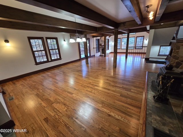 unfurnished living room featuring baseboards, wood finished floors, beam ceiling, and a chandelier