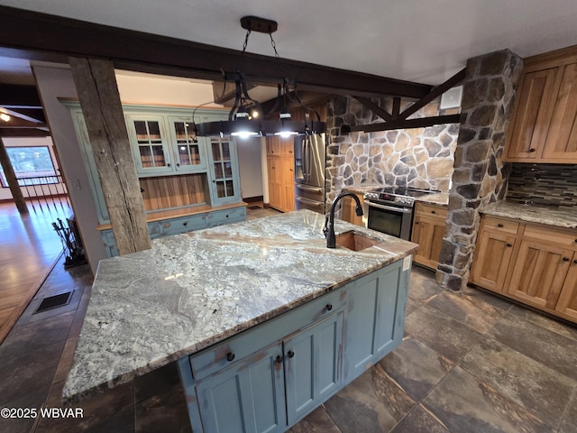 kitchen with light stone counters, visible vents, a kitchen island with sink, a sink, and appliances with stainless steel finishes