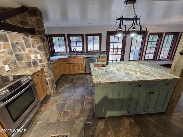 kitchen with light stone countertops, appliances with stainless steel finishes, hanging light fixtures, stone finish floor, and a sink