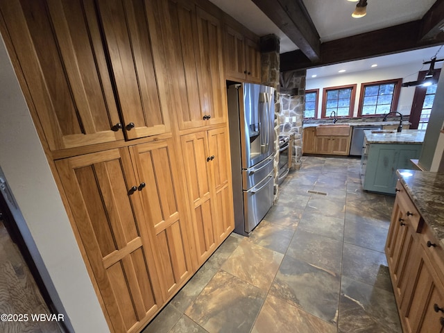 kitchen featuring beamed ceiling, stone finish floor, stone countertops, stainless steel appliances, and a sink