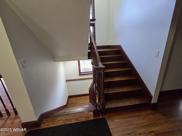 stairway featuring lofted ceiling, baseboards, and wood-type flooring