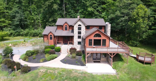 view of front facade with driveway, a front lawn, stone siding, a wooden deck, and a chimney