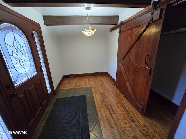 entryway with beamed ceiling, baseboards, a barn door, and wood finished floors