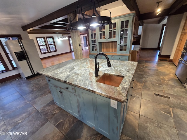 kitchen featuring glass insert cabinets, baseboards, beamed ceiling, white fridge with ice dispenser, and a sink