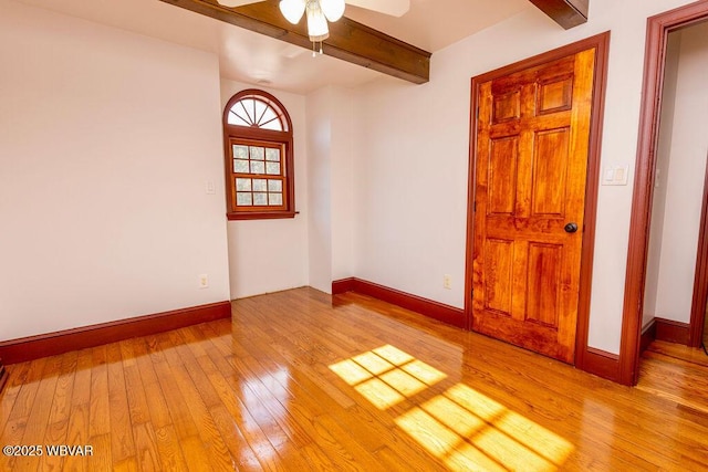 empty room with ceiling fan, baseboards, beam ceiling, and light wood-style flooring