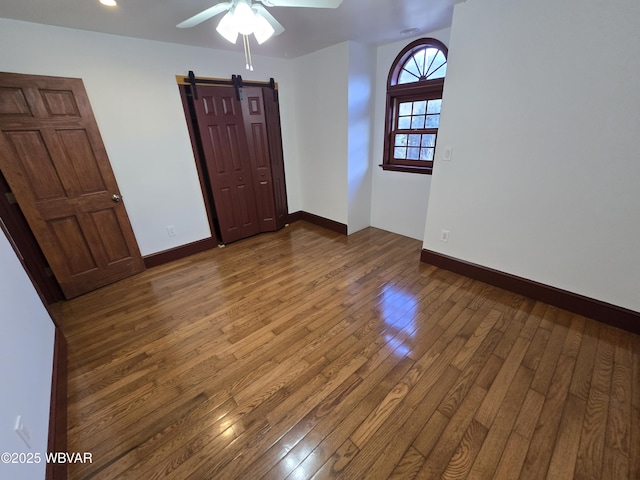 spare room featuring a barn door, wood-type flooring, baseboards, and a ceiling fan