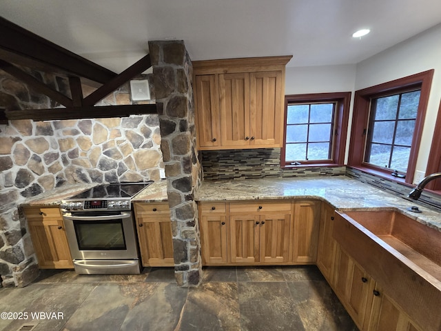 kitchen with electric range, light stone counters, tasteful backsplash, and a sink