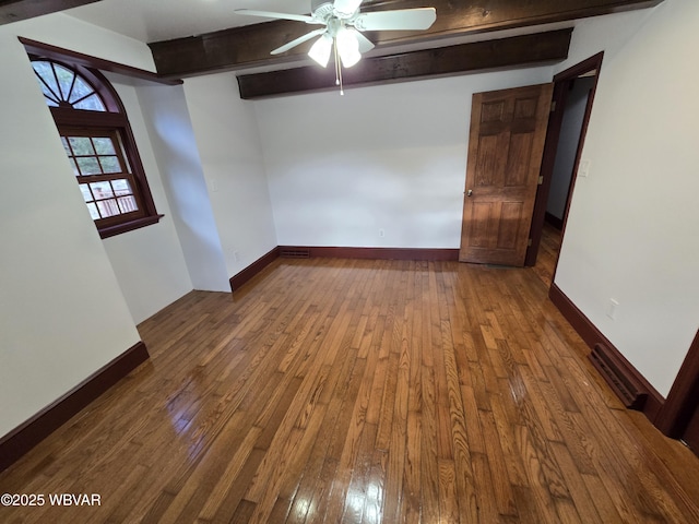 empty room with dark wood finished floors, beamed ceiling, and baseboards