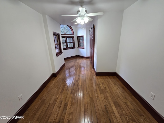 interior space with a barn door, dark wood-style floors, baseboards, and ceiling fan