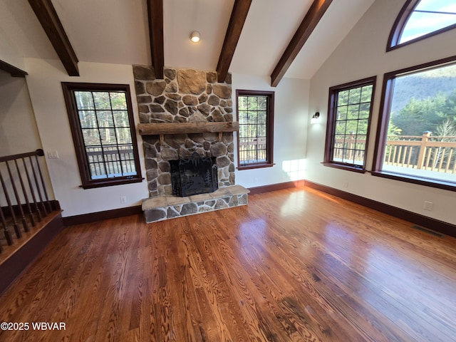 unfurnished living room with visible vents, vaulted ceiling with beams, baseboards, a stone fireplace, and wood finished floors