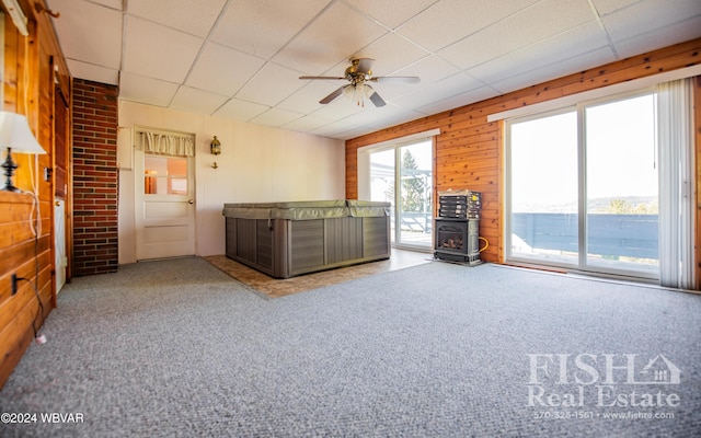 unfurnished living room featuring a drop ceiling, ceiling fan, light colored carpet, and wooden walls