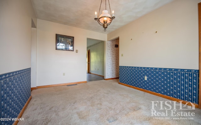 carpeted empty room with a notable chandelier