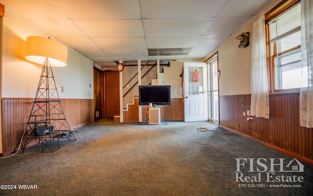 unfurnished living room featuring carpet flooring, a drop ceiling, and wood walls