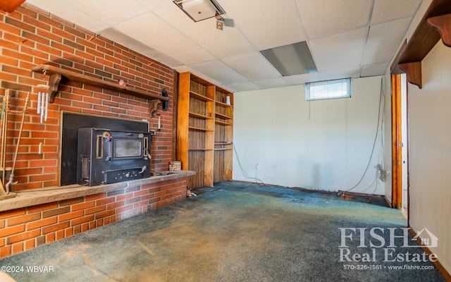 unfurnished living room featuring a paneled ceiling, a wood stove, and dark colored carpet