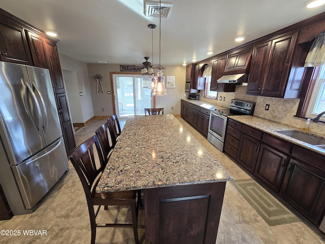 kitchen with appliances with stainless steel finishes, a breakfast bar, sink, pendant lighting, and a kitchen island