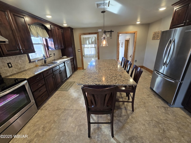 kitchen featuring a breakfast bar area, light stone countertops, decorative light fixtures, and appliances with stainless steel finishes