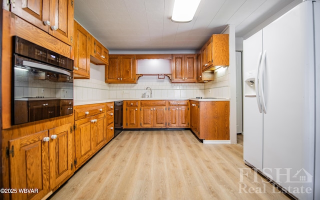 kitchen featuring brown cabinets, a sink, light wood-type flooring, backsplash, and black appliances